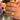 Hand wearing a gold plated ring with a enamel design in front of colorful flowers
