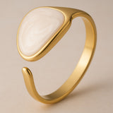 Adjustable gold plated ring with a white liquid enamel on a beige background