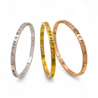 Three bracelets with Roman numeral designs in gold plated, rose gold plated and stainless steel, on a white background