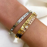 Three bracelets with Roman numeral designs on a wrist against a white background