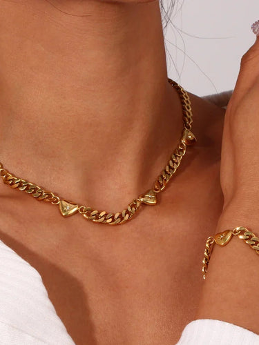 Gold plated cuban with heart chain and bracelet on a person wearing a white top.