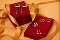 Pair of earrings on red velvet boxes with gold ribbons on a beige background