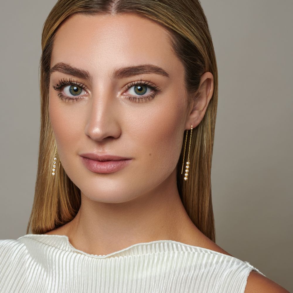 Close-up of a woman with long blonde hair wearing gold plated silver drop earrings against a neutral background