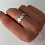 Hand wearing a gold plated heart cuff ring with white liquid enamel on a plain background