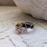Set of two heart-shaped cuff rings in gold, silver, and black on a textured surface.