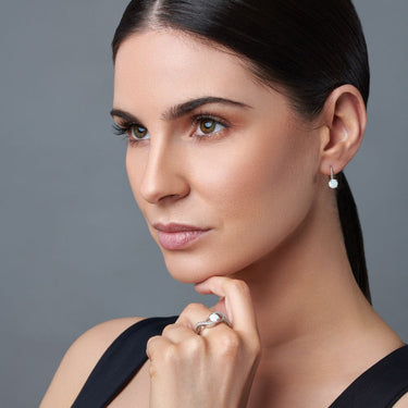 Close-up of our murban pizazz model wearing opal earrings and a ring against a gray background