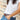 Person wearing a custom gold name bracelet with a white t-shirt, blue jeans, and a brown belt with a wooden background.