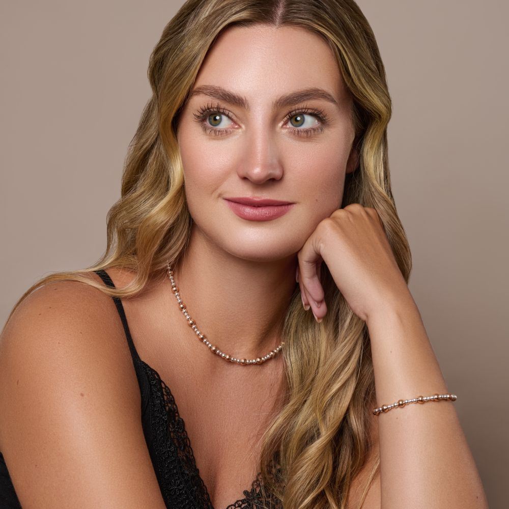 Urban Pizazz model Woman wearing Rose Gold Plated beaded necklace and bracelet against a beige background