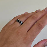 Hand wearing a stainless steel heart cuff ring with black liquid enamel on a plain background