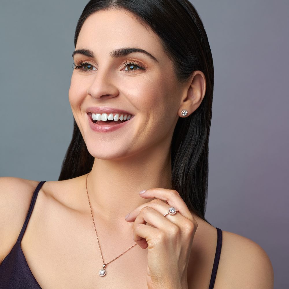 Woman wearing rose gold plated necklace, ring and earrings against a gray background