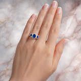 Hand wearing a ring with blue gemstones on a marble background