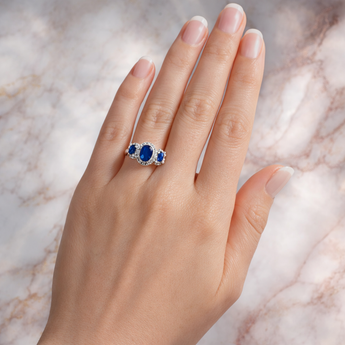 Hand wearing a ring with blue gemstones on a marble background
